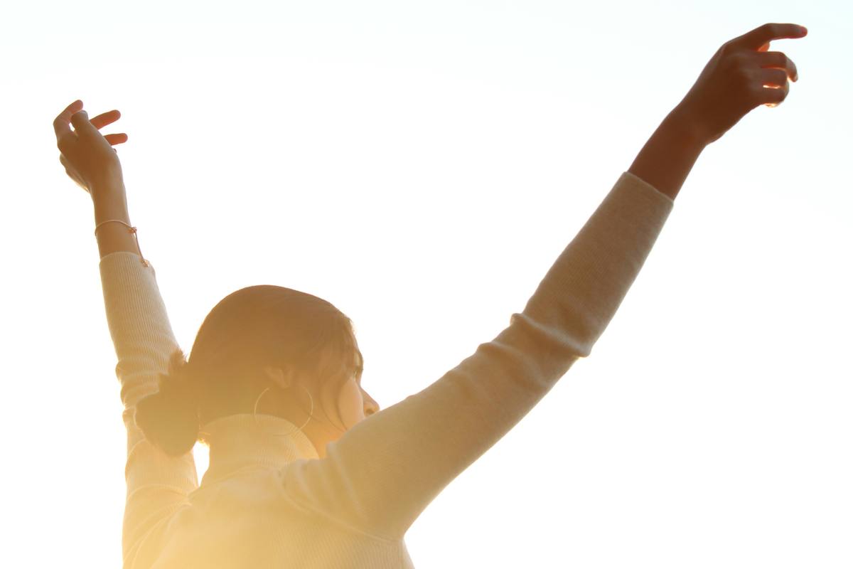 Woman with arms raised toward the sunlit sky, reaching into her next chapter